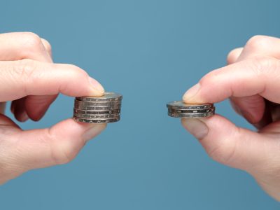Hands are comparing two stacks of coins of different sizes, indicating worsening financial situation
