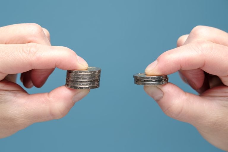 Hands are comparing two stacks of coins of different sizes, indicating worsening financial situation