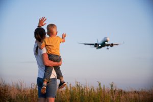 Woman with child waving hand to landing commercial airplane